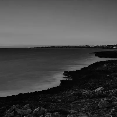 A black-and-white photograph of a rocky coastline, from the original website.
